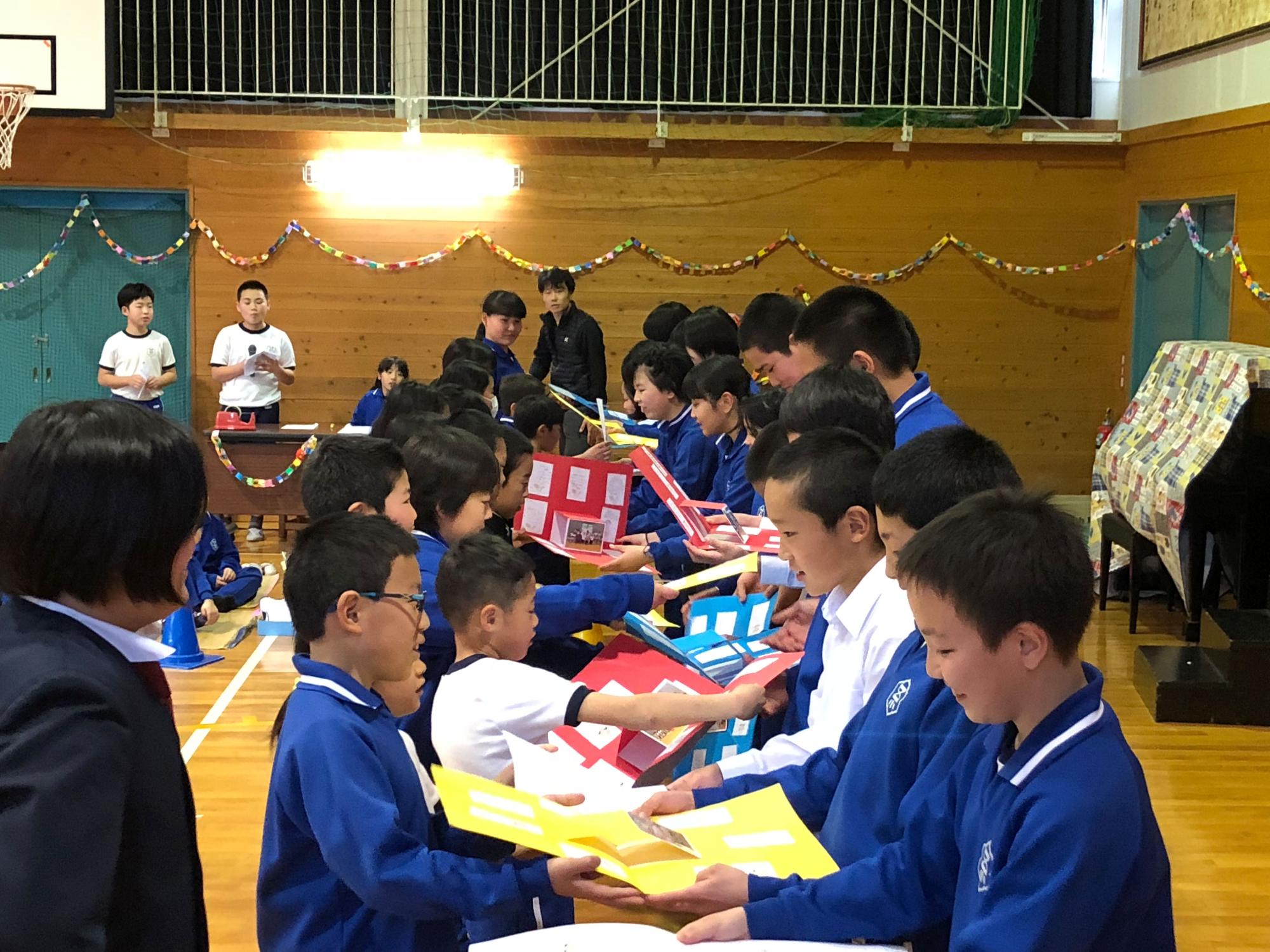 下級生の児童から6年生の児童にプレゼントを渡している写真