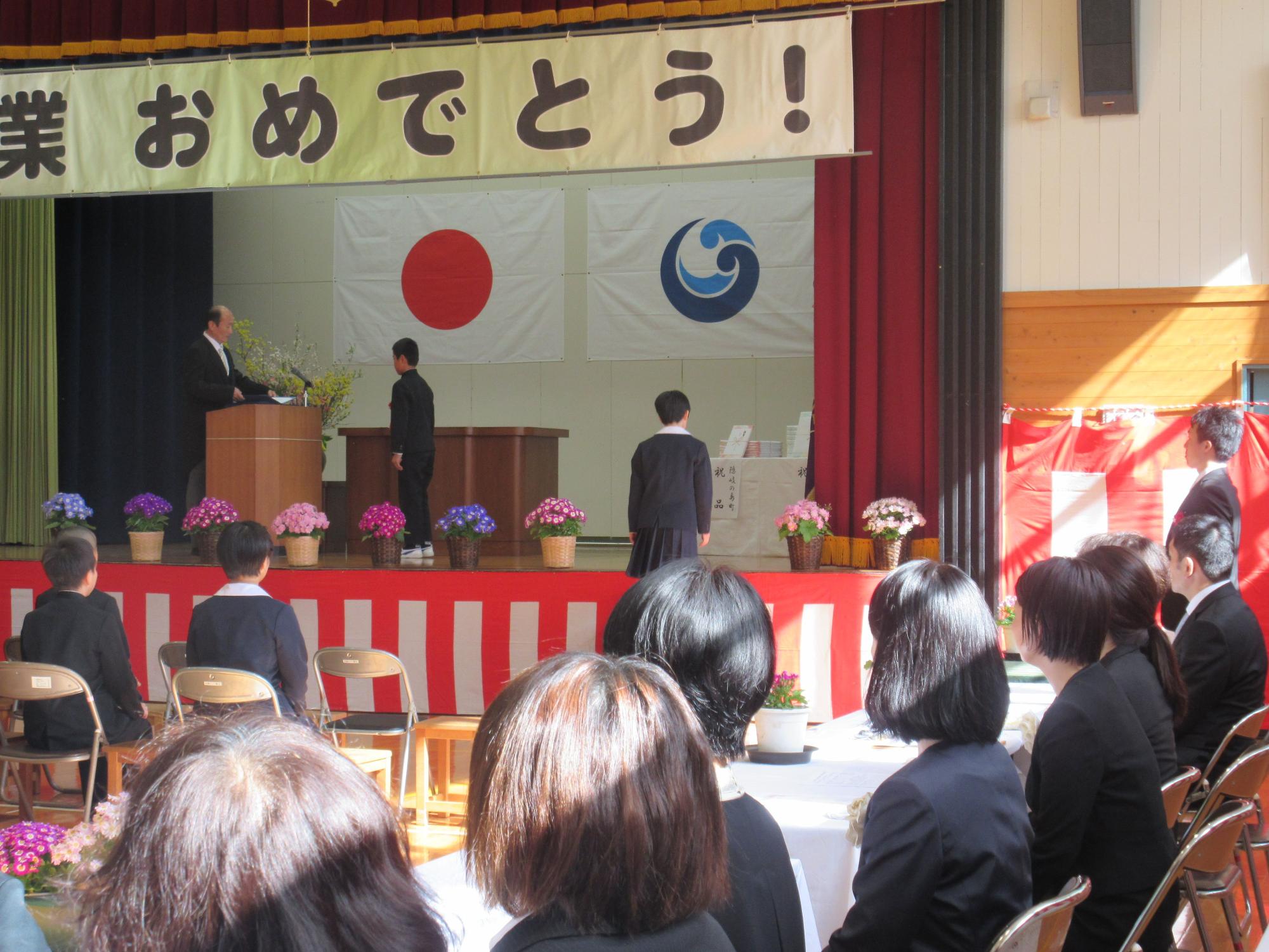 ステージで校長先生から卒業証書を受け取っている卒業生の写真
