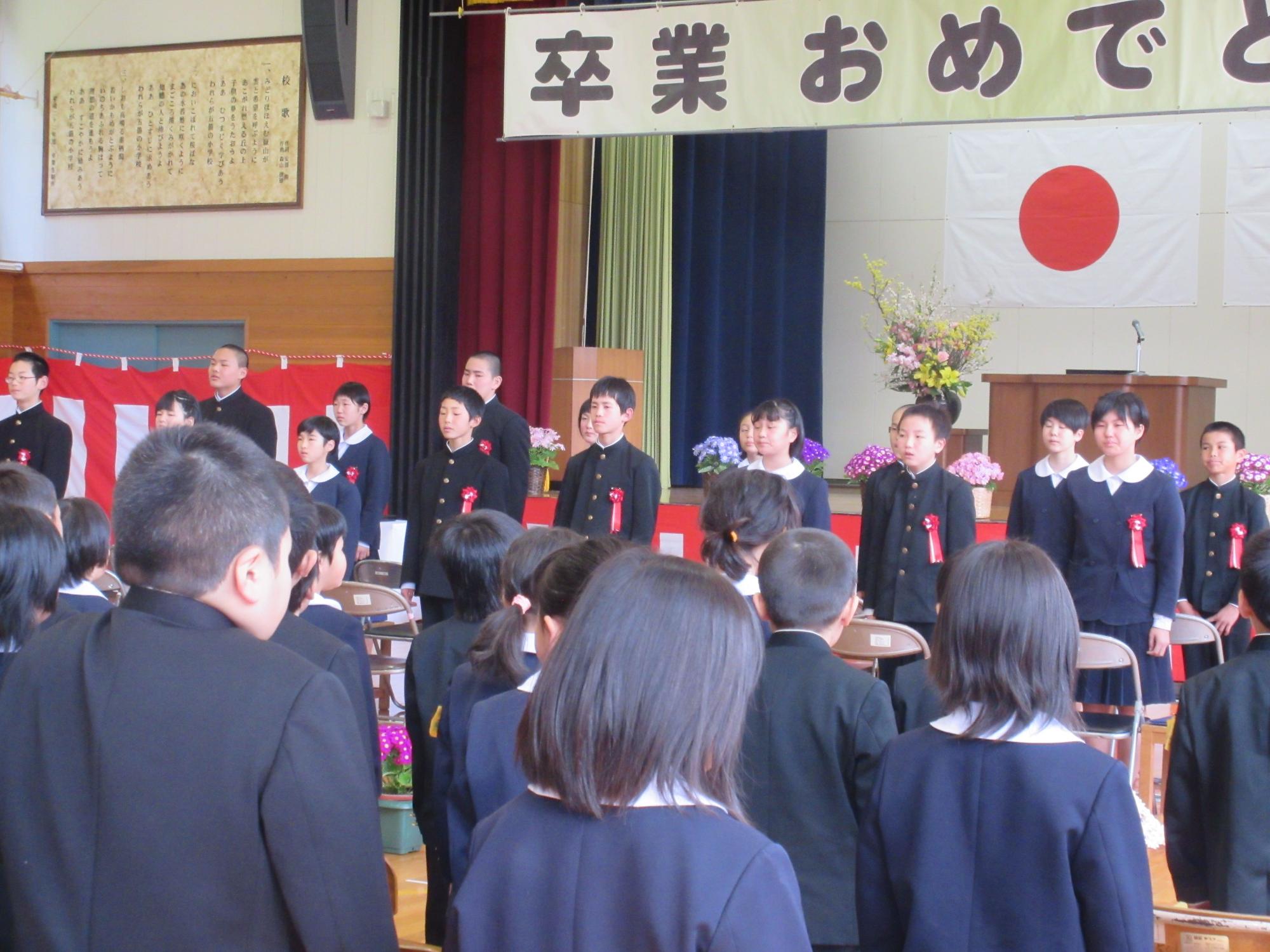卒業生が在校生の方を向いて横一列に並んでいる写真