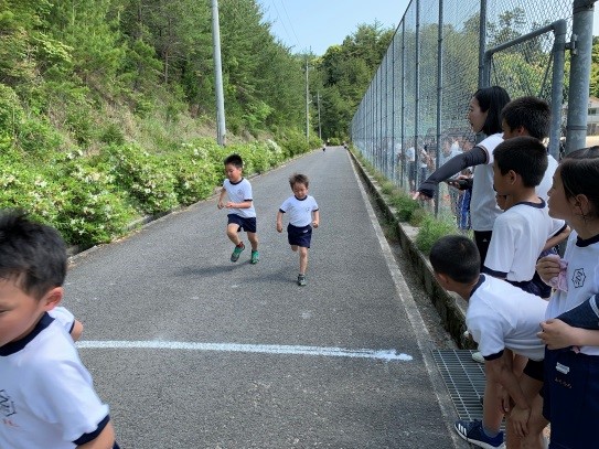 体操着姿の児童が道路のゴールラインに向かって走っている写真