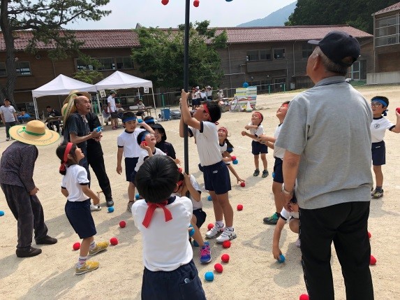 体操着姿の児童たちと大人たちが玉入れをしている写真