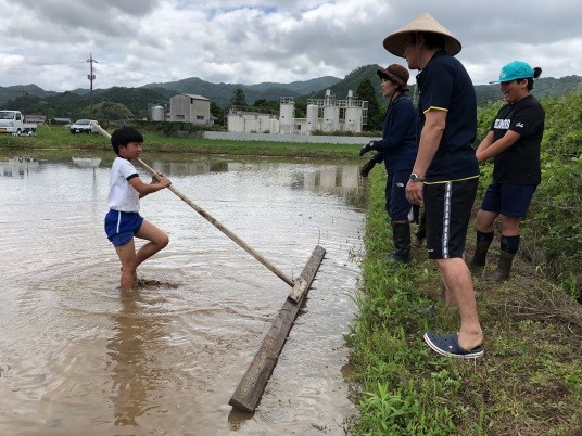 体操着姿の児童がばば引きをしている姿を大人が見守っている写真