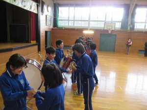 体育館で太鼓や楽器を前に児童たちが向かい合い並んでいる写真