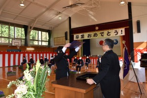 体育館で卒業証書を受け取る児童と、壇上に立つ男性が向かい合っている写真
