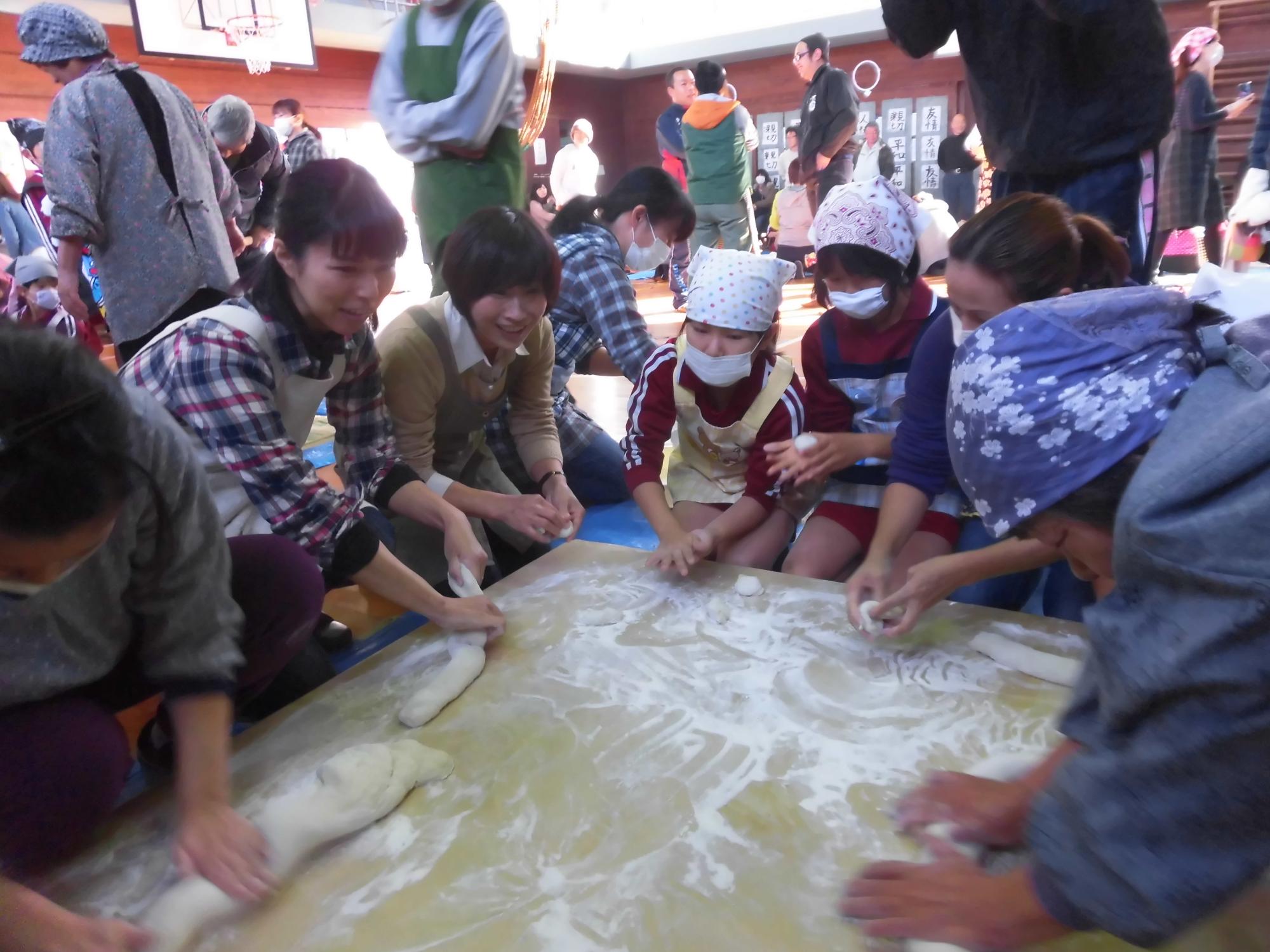 体育館で児童や大人が餅をこねている写真