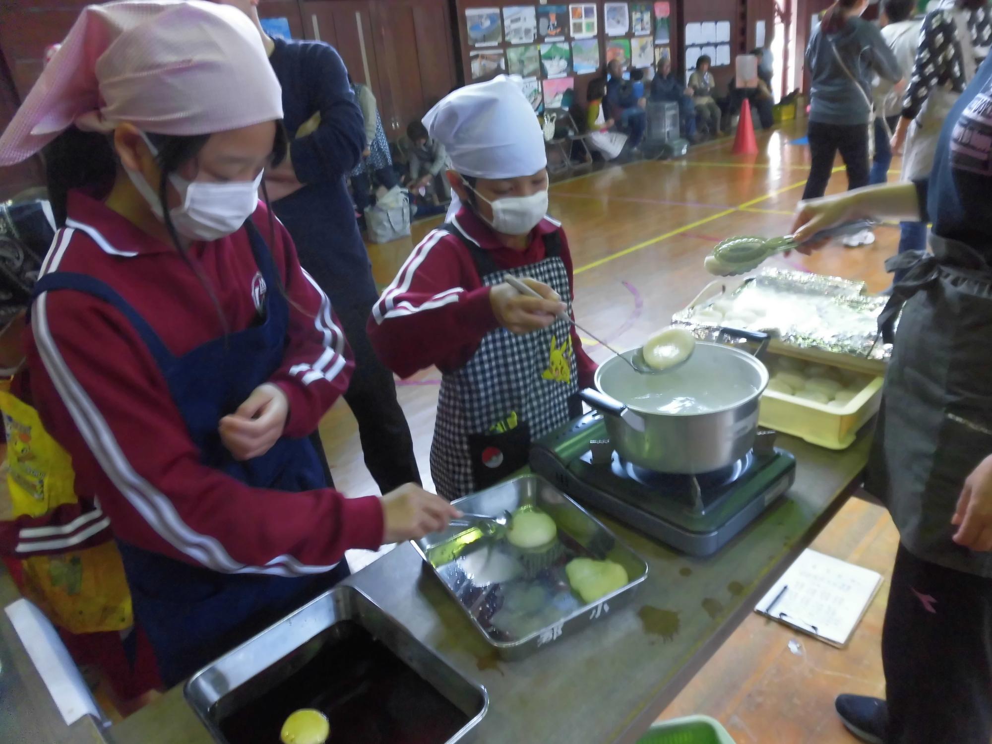 三角巾を被った2人の児童が鍋で餅を茹でている写真