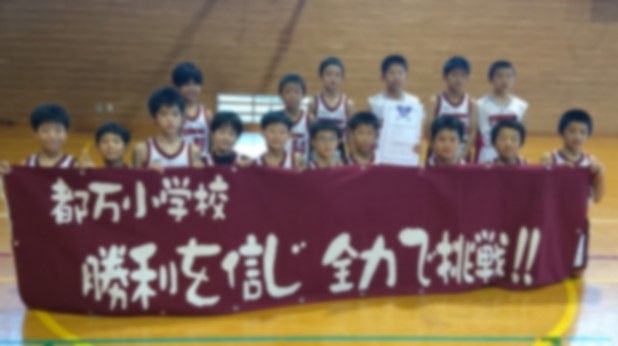 体育館でユニフォームを着た男子児童が横断幕を持ち並んでいる写真