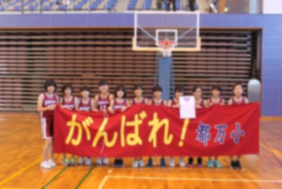 体育館でユニフォームを着た女子児童が横断幕を持ち並んでいる写真