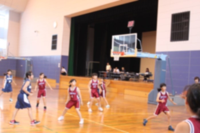 体育館でユニフォームを着た女子児童がバスケットボールの試合をしている写真