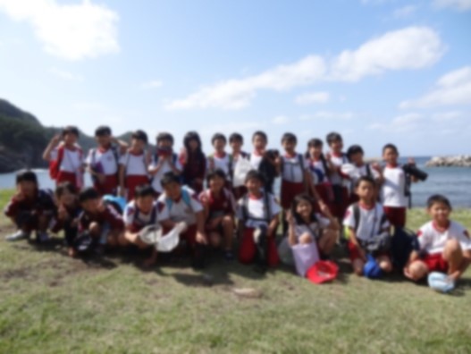 秋季遠足で水辺に児童が集まり前列が座って記念撮影をしている写真