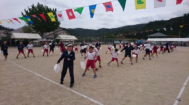 校庭で児童が旗の下でポンポンを持って踊っている写真