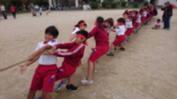 校庭で赤いハチマキをした児童が綱引きをしている写真