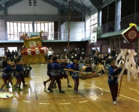 体育館で児童が神輿を担いで歩いている写真