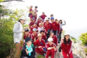 山の岩場のような場所で先生と児童たちが記念撮影をしている写真