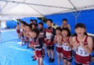 テントの下で応援しているユニフォーム姿の児童たちの写真