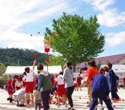 体育大会でで児童と大人が一緒に玉入れをしている写真