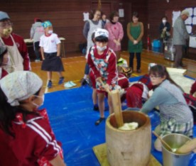 児童たちが杵で餅をつき、大人が支えている写真