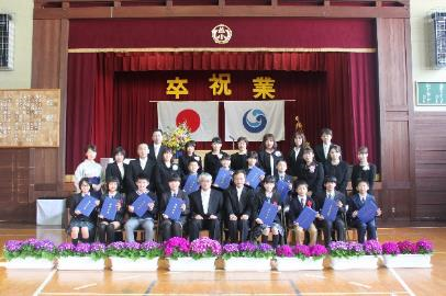 卒業生と教職員がステージ前で記念撮影している写真