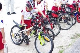 ヘルメットををかぶり、自転車の横に立っている児童の写真