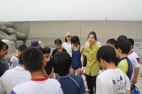 児童たちが環境省の人の周りに立ち、お話を聞いている写真