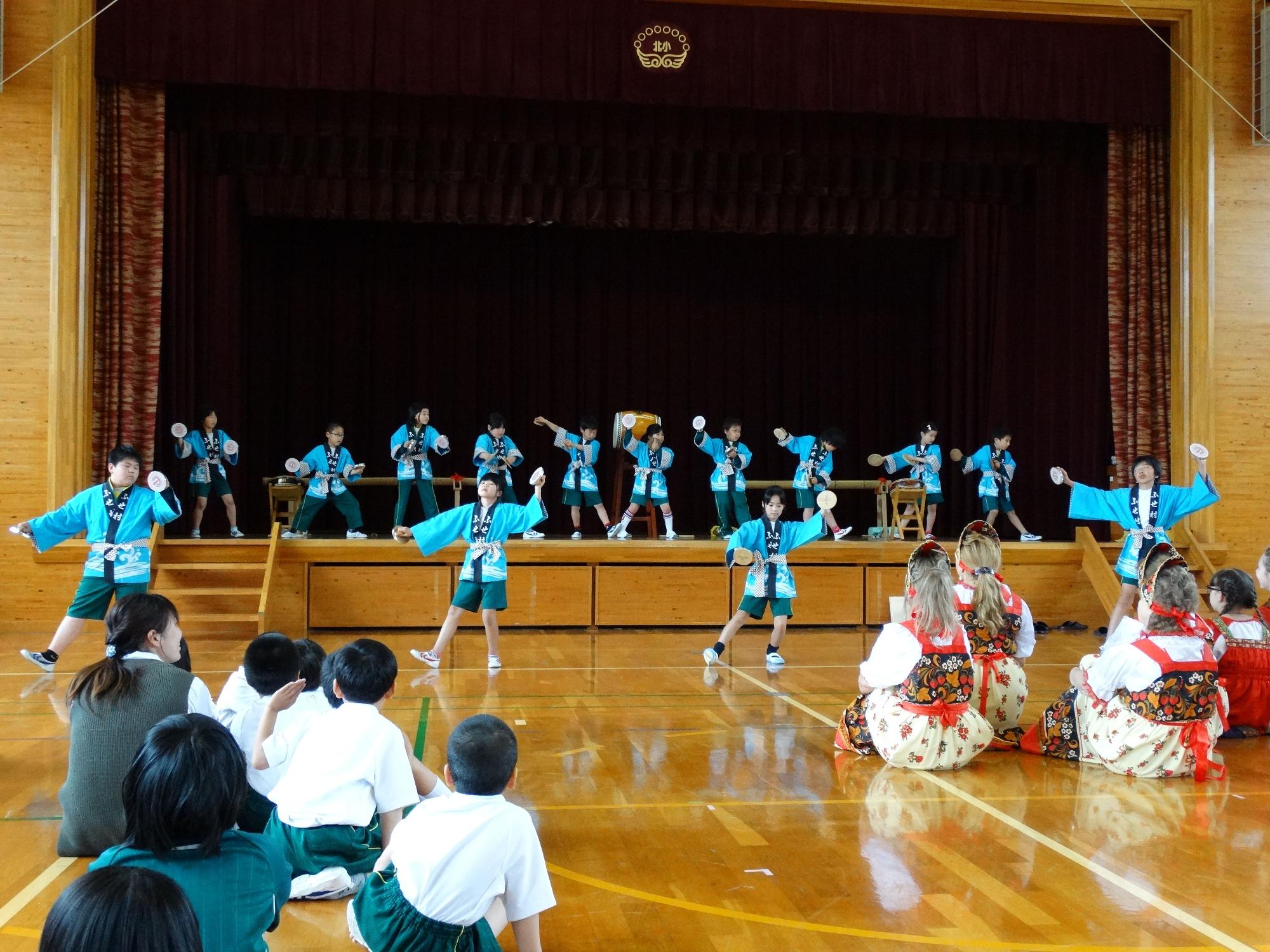 体育館のステージ上で法被姿の児童が踊りを踊っている写真