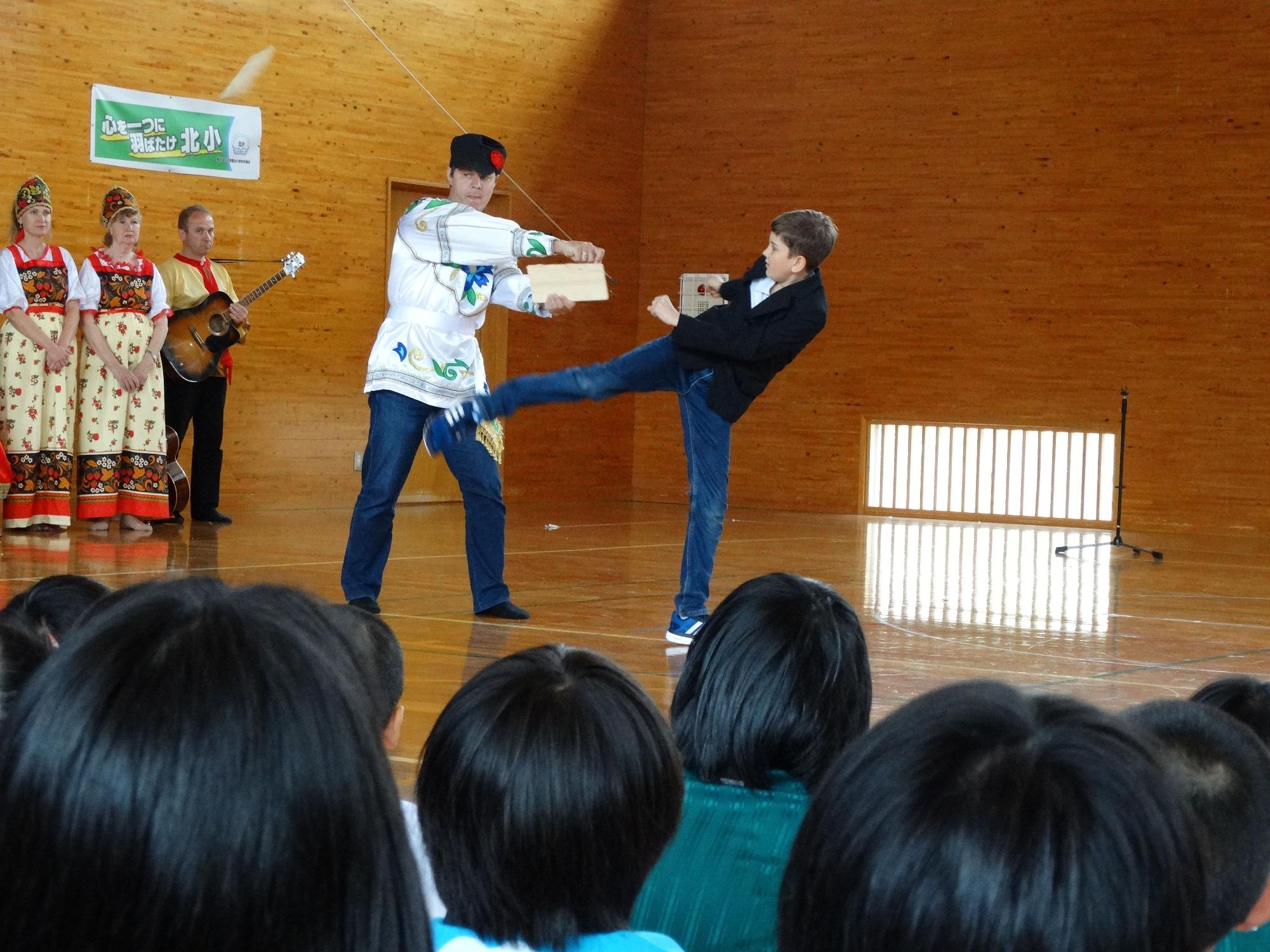 体育館で外国の子供が板割りのパフォーマンスを披露している写真