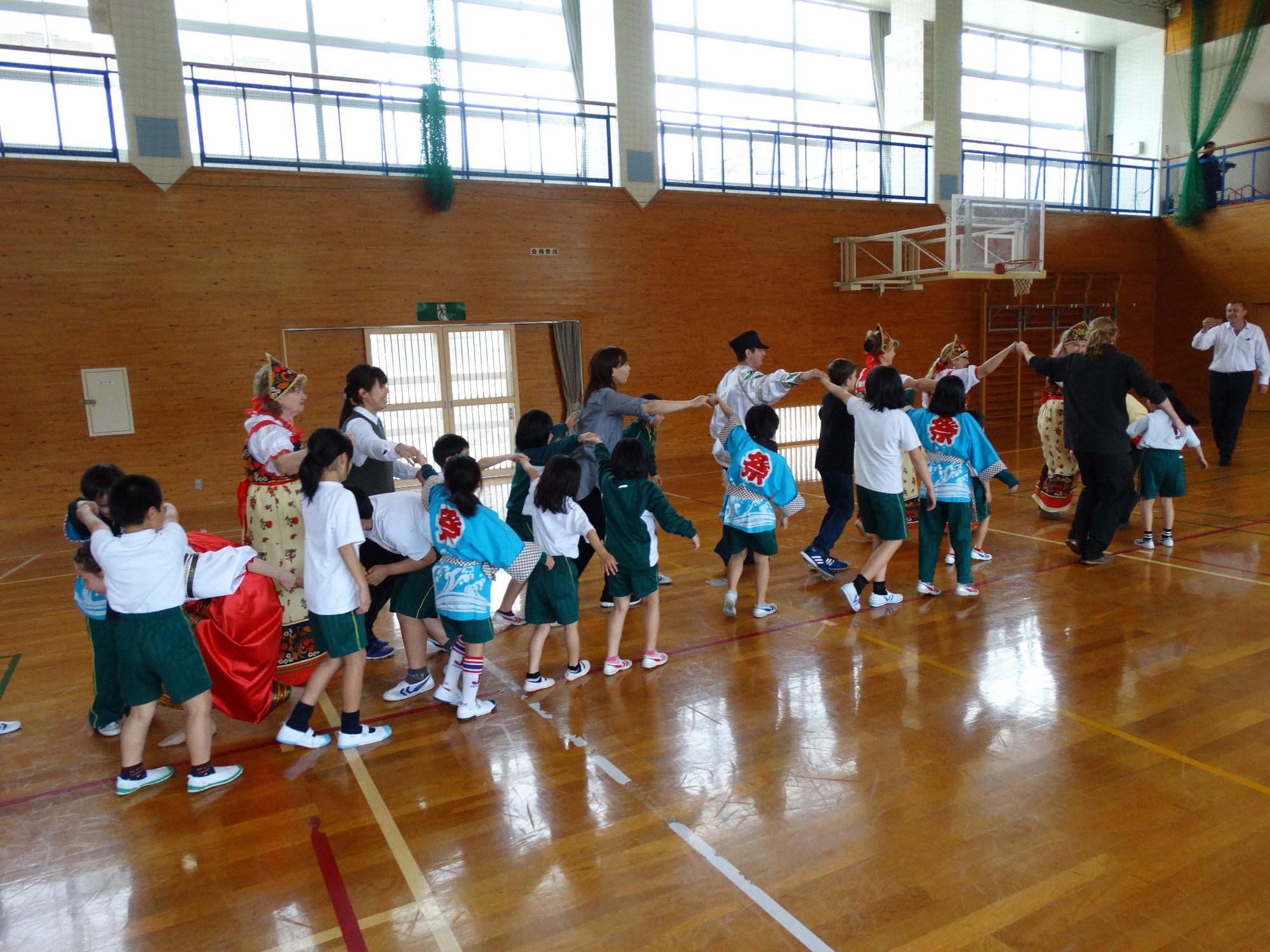 体育館で児童と外国の来訪者が手を繋いでいる写真