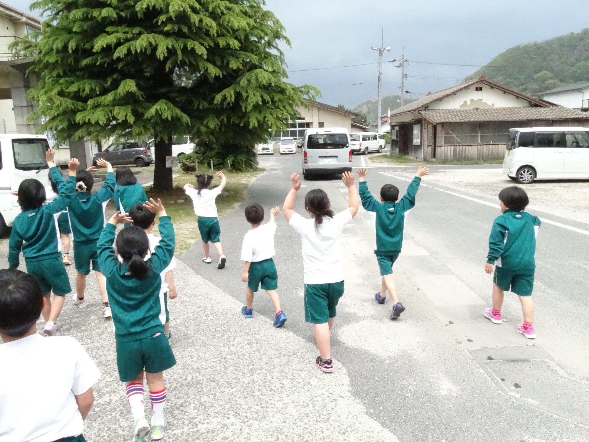 走り去る車に手を振って見送る児童たちの後ろ姿の写真