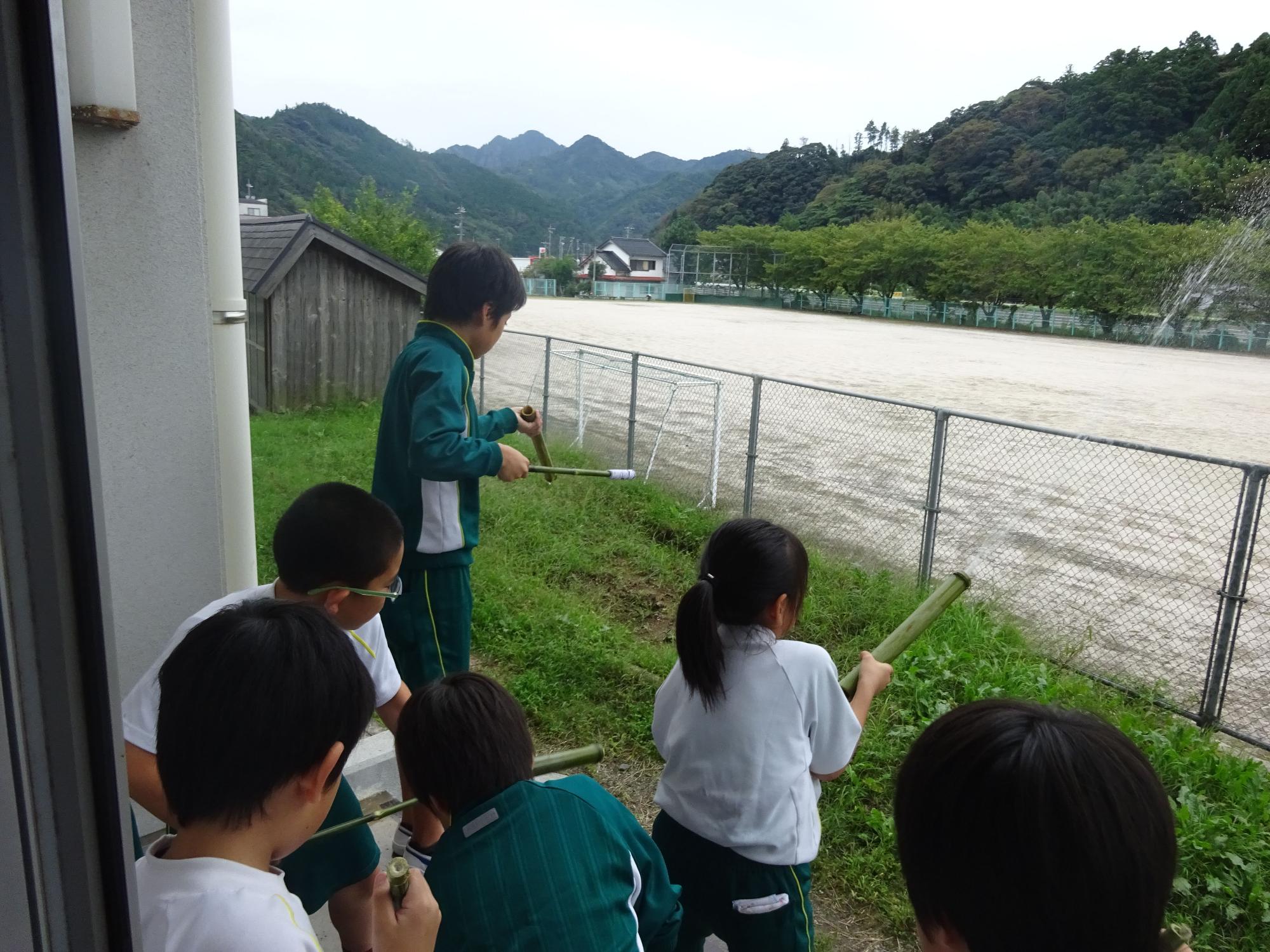 児童たちが水鉄砲のようなものをグラウンドに向けて使っている写真