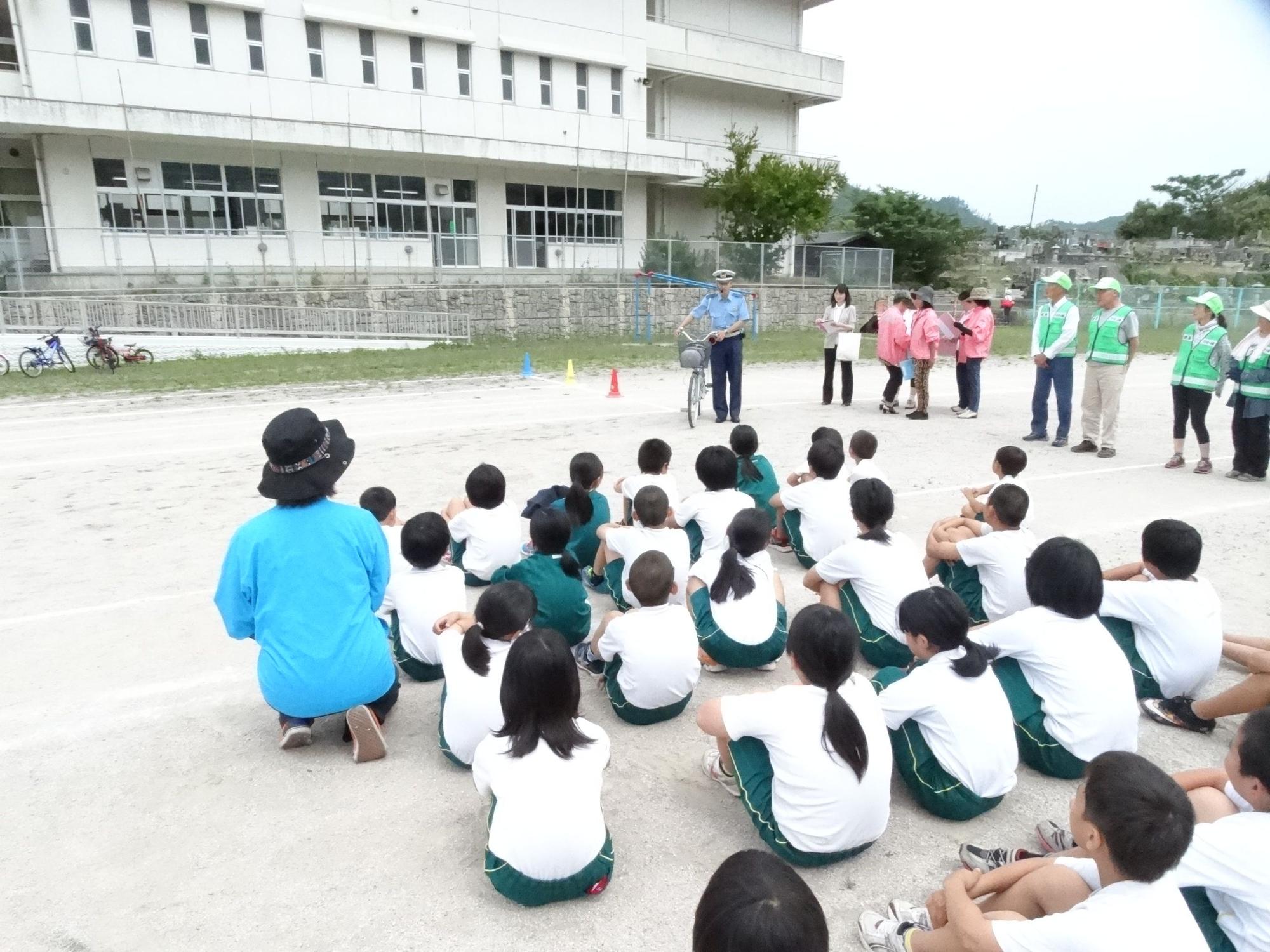 校庭に整列して座って説明を聞いている児童たちの写真
