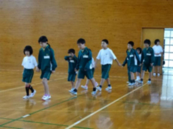 一年生と上級生が手をつないで体育館を歩いている写真