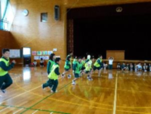ビブスを着けた児童たちが体育館で遊んでいる写真