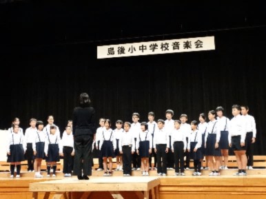 舞台で三年生から六年生の児童が整列し合唱している写真