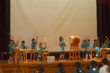 舞台で児童が法被を着て和太鼓を演奏している写真