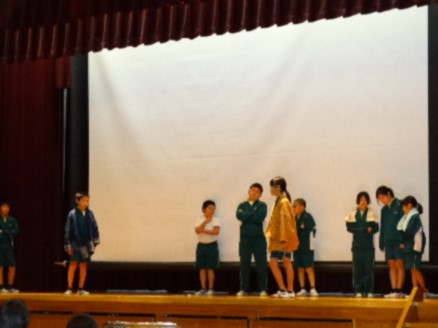 舞台で児童が立ち、悩むポーズをして演技している写真