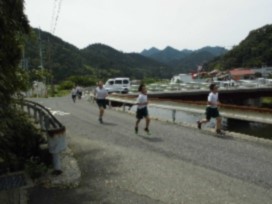 晴天の中川沿いの道を複数の児童たちが一生懸命走っている写真