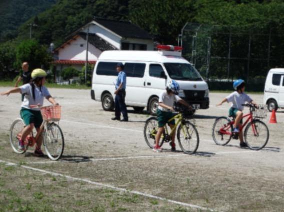 小学校の校庭で数人の生徒が各々の自転車にまたがり、手信号の練習をしている写真