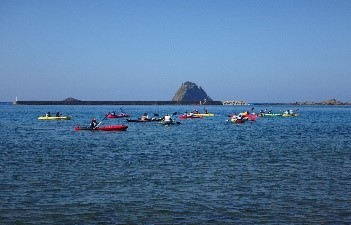 穏やかな海で児童たちがシーカヤックを漕いでいる写真