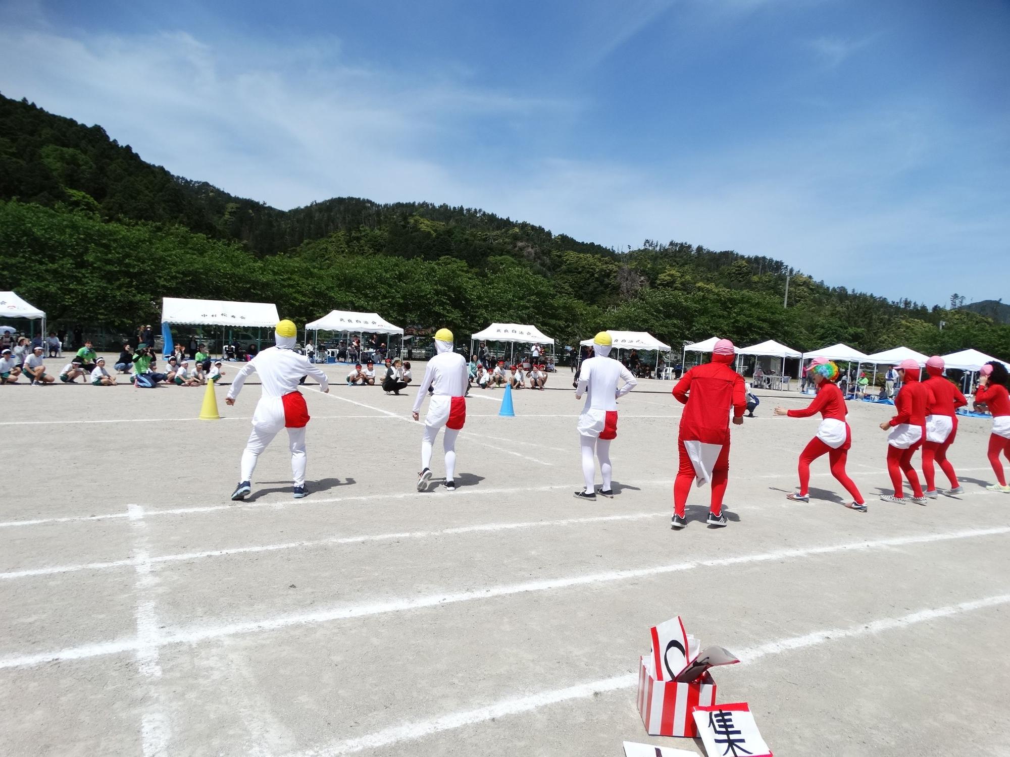 青空の下小学校の校庭で地域の方々が白色や赤色のコスチュームを着てダンスを披露している写真