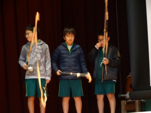 体操服姿の3人の児童が弓のようなものを手に持ち並んでいる写真