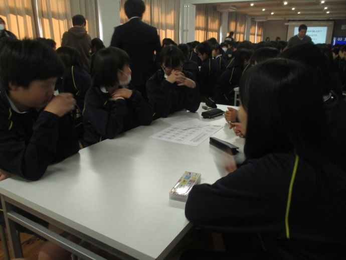 生徒が複数の机を囲んで座り、中央の用紙を見ながら話している写真