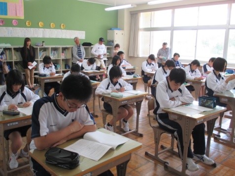 教室で授業に取り組んでいる生徒の様子を後ろから大人が見守っている写真