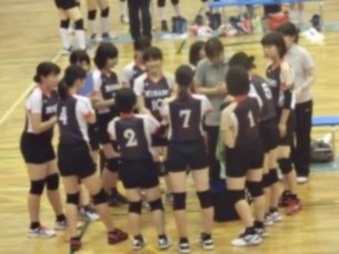 室内のコートでバレーボールのユニフォームを着た生徒たちが円になって話し合っている写真