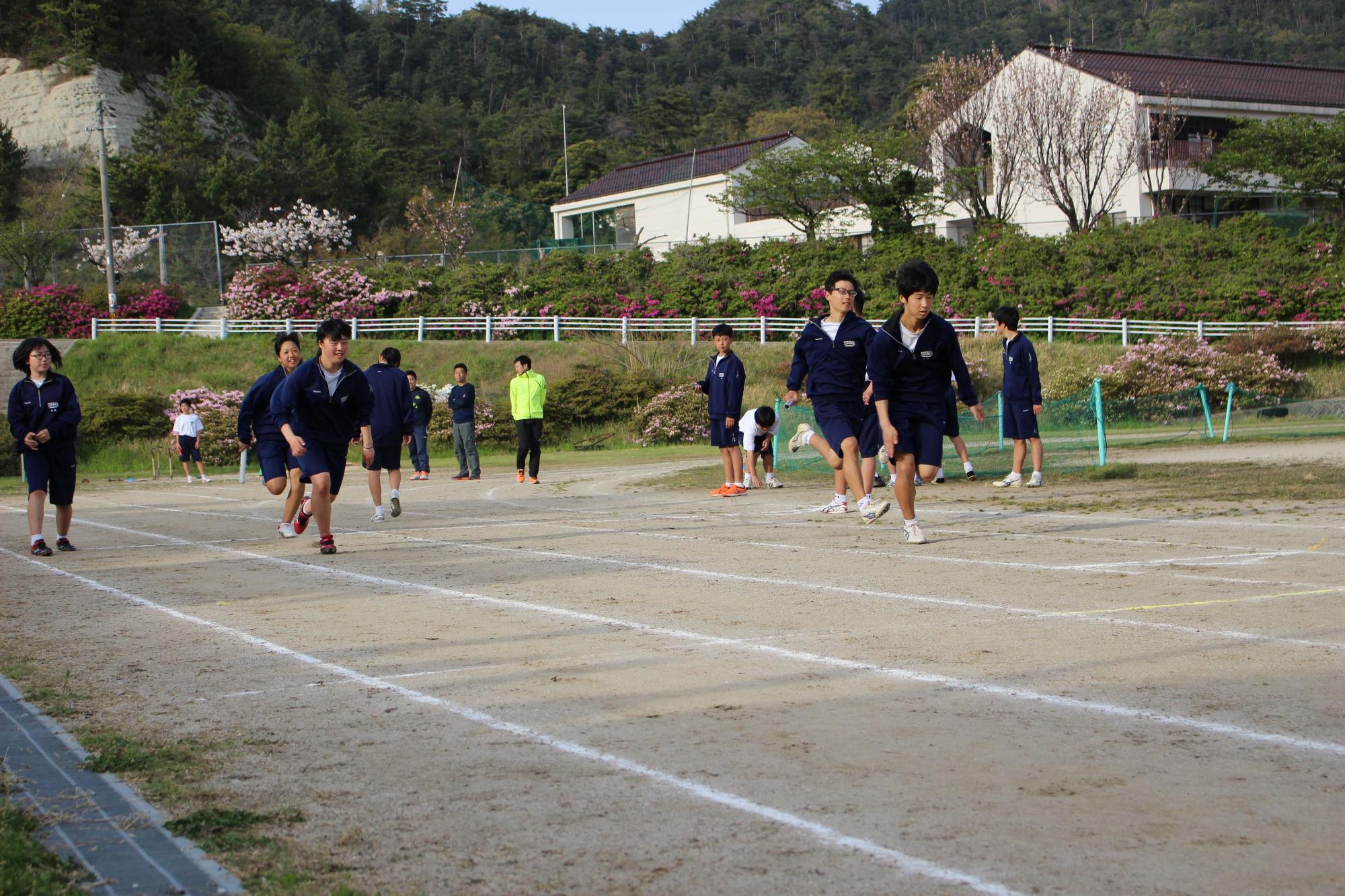 校庭のコースをジャージ姿の生徒たちが走っている写真