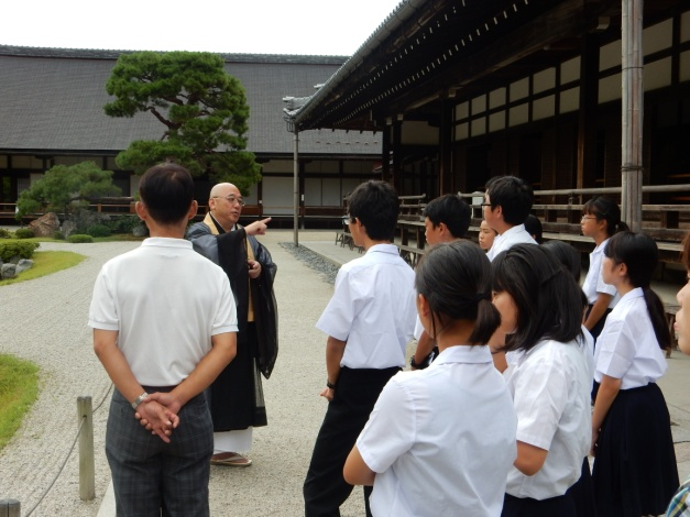 寺院内で僧侶の方のお話しを複数の生徒が聞いている写真