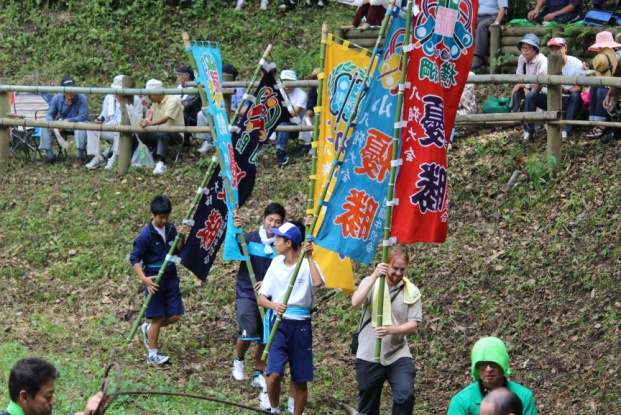 複数の児童や大人が大きな旗を持って歩いている写真