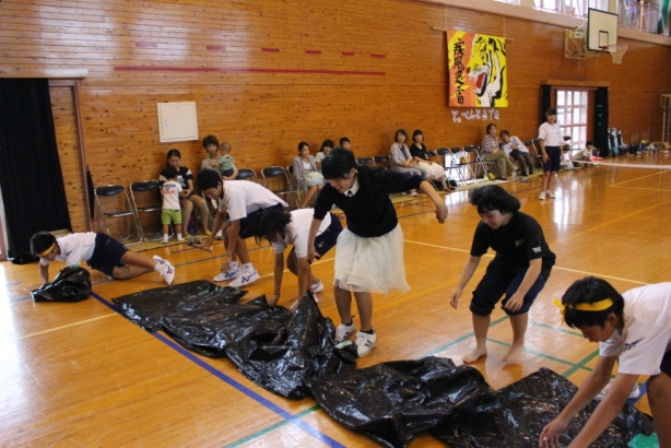 体育館で生徒たちがビニールシートのようなものを床に置いて競技を行っている写真