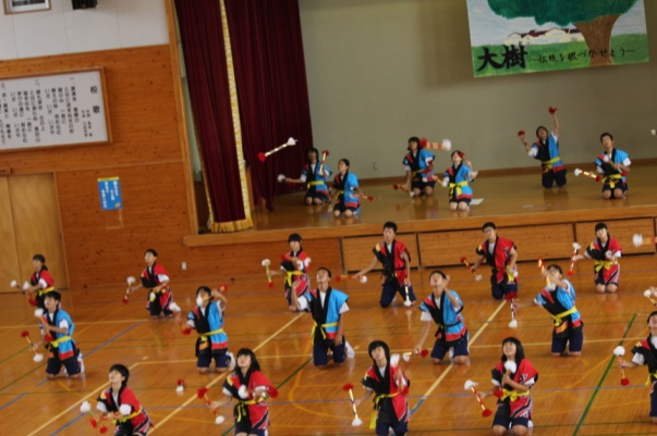 体育館で法被姿の生徒たちが手にけん玉のようなものを持ちながら一斉に空中に投げている写真