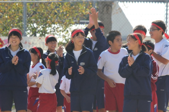 ハチマキ姿の生徒や児童が笑顔で手を叩いている写真