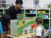 段ボールと紙で作った模型を保育園児に見せている生徒の写真
